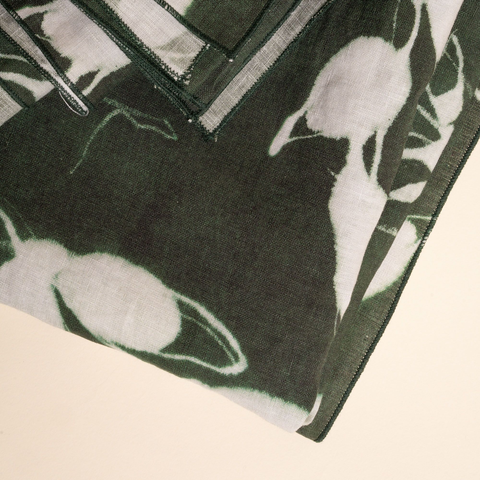 A closeup of a folded tablecloth in a dark green color with white botanical print on a neutral background.