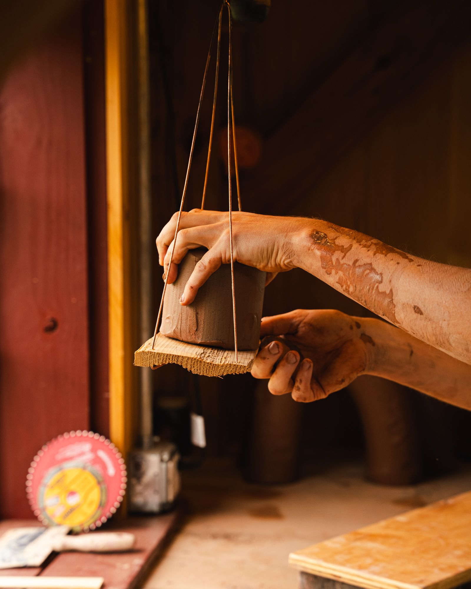 John measures a block of clay on a scale hanging in a window