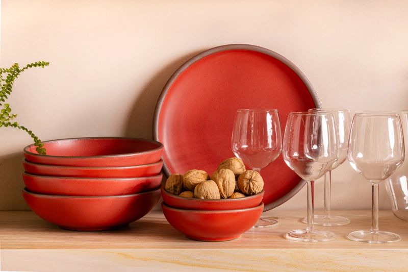 A shelf with ceramic bold red plates and bowls with wine glasses