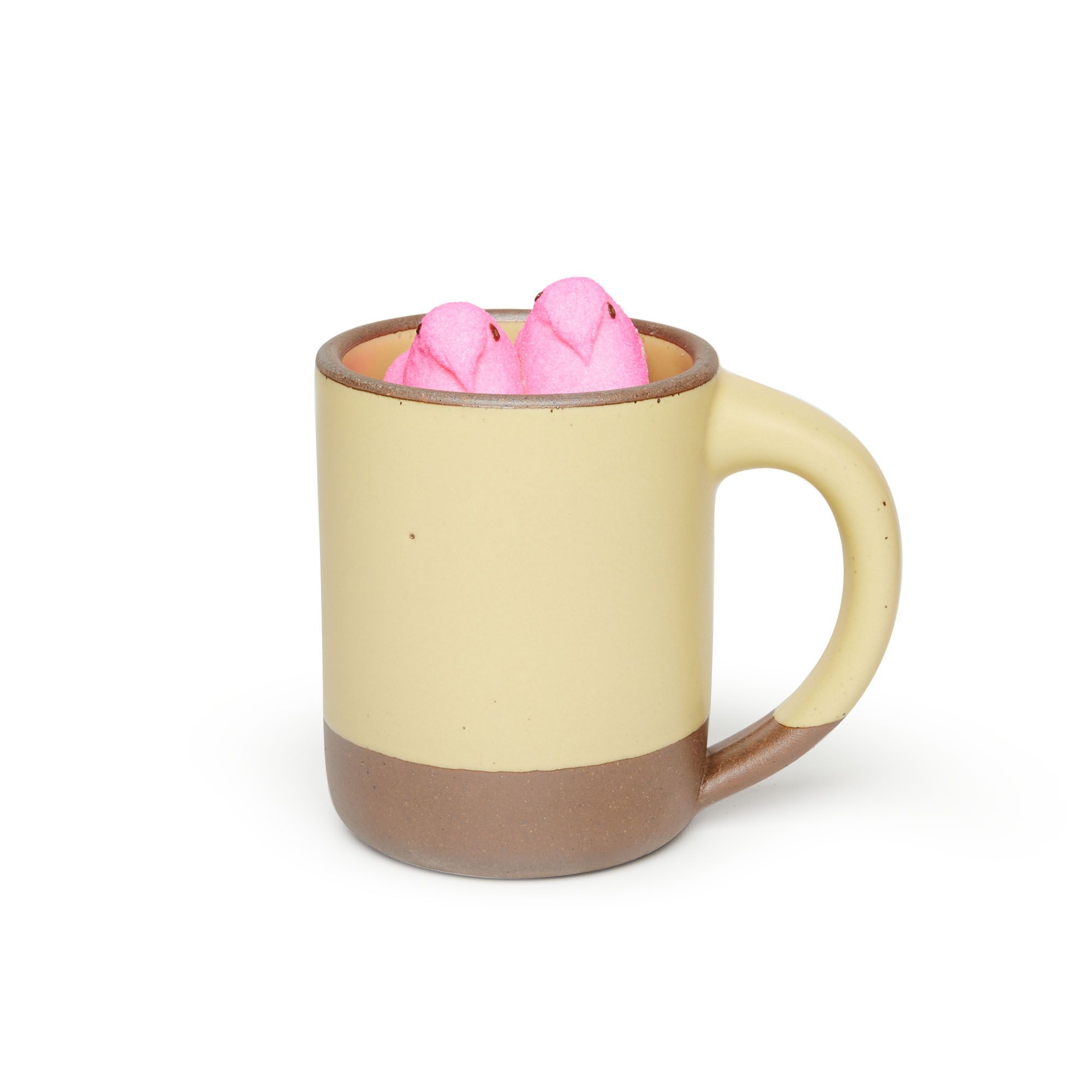 A big sized ceramic mug with handle in a light butter yellow glaze featuring iron speckles and unglazed rim and bottom base, with 2 pink candy peeps inside