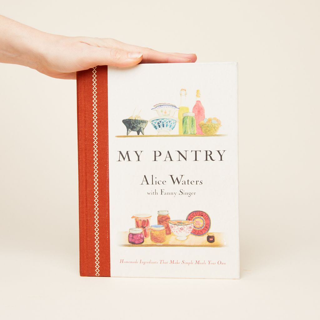 A hand lies along the top of the cookbook My Pantry by Alice Waters