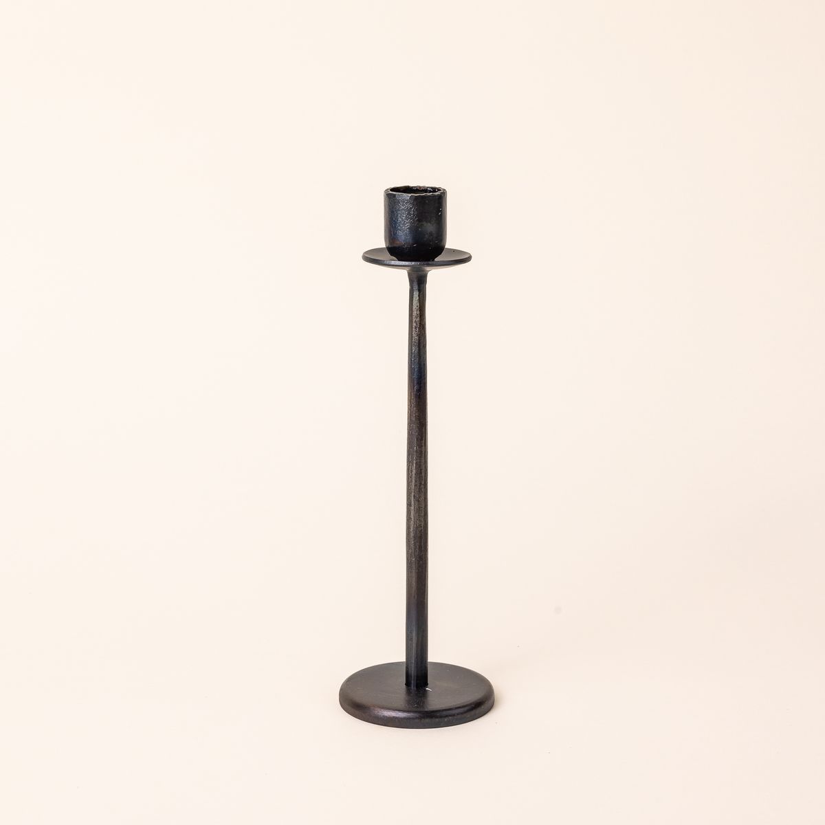 Tall narrow iron candlestick holder with a flat circle base and topped with a simple taper candle holder.