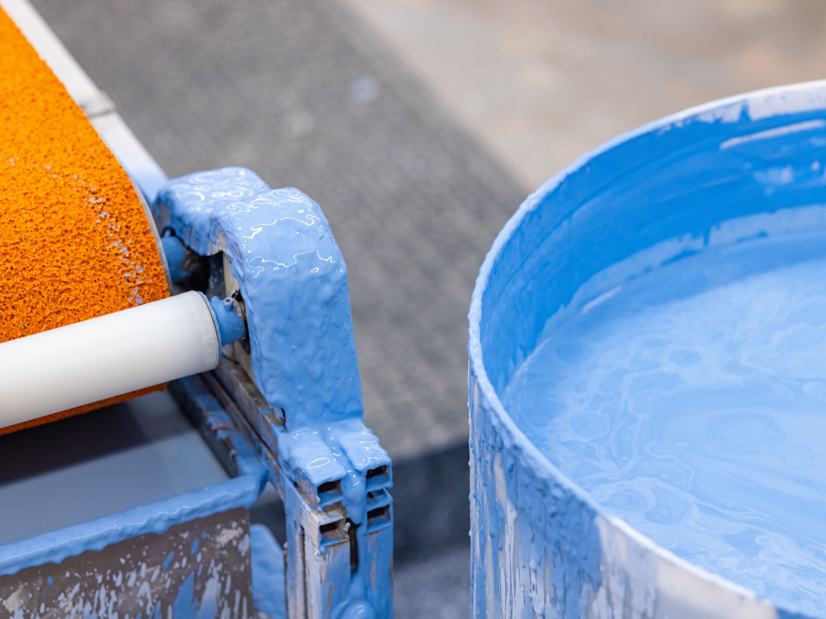Ceramic glazing machinery and a tub of light blue glaze on the factory floor.