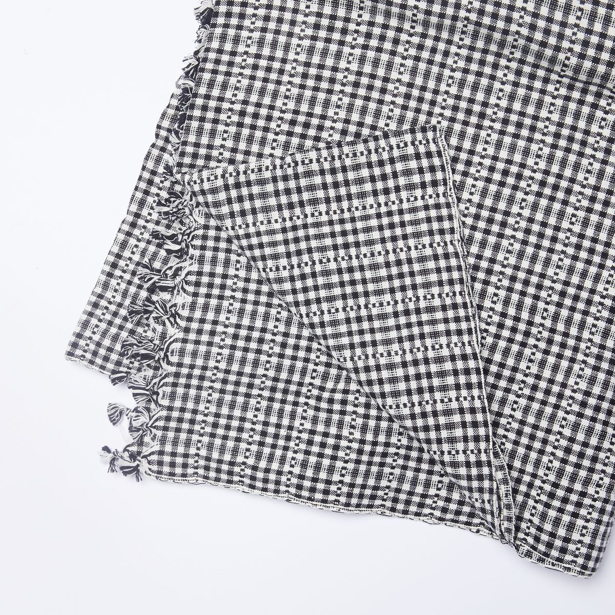 A folded black and white gingham cotton tablecloth with one corner pulled back