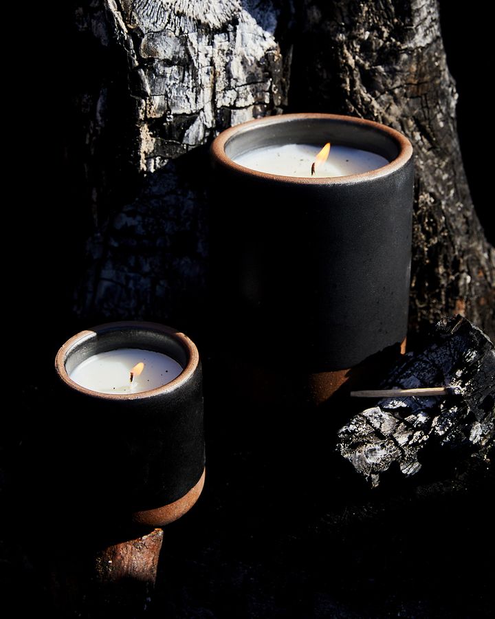 Large and small ceramic black candles lit in an earthy dark tree setting