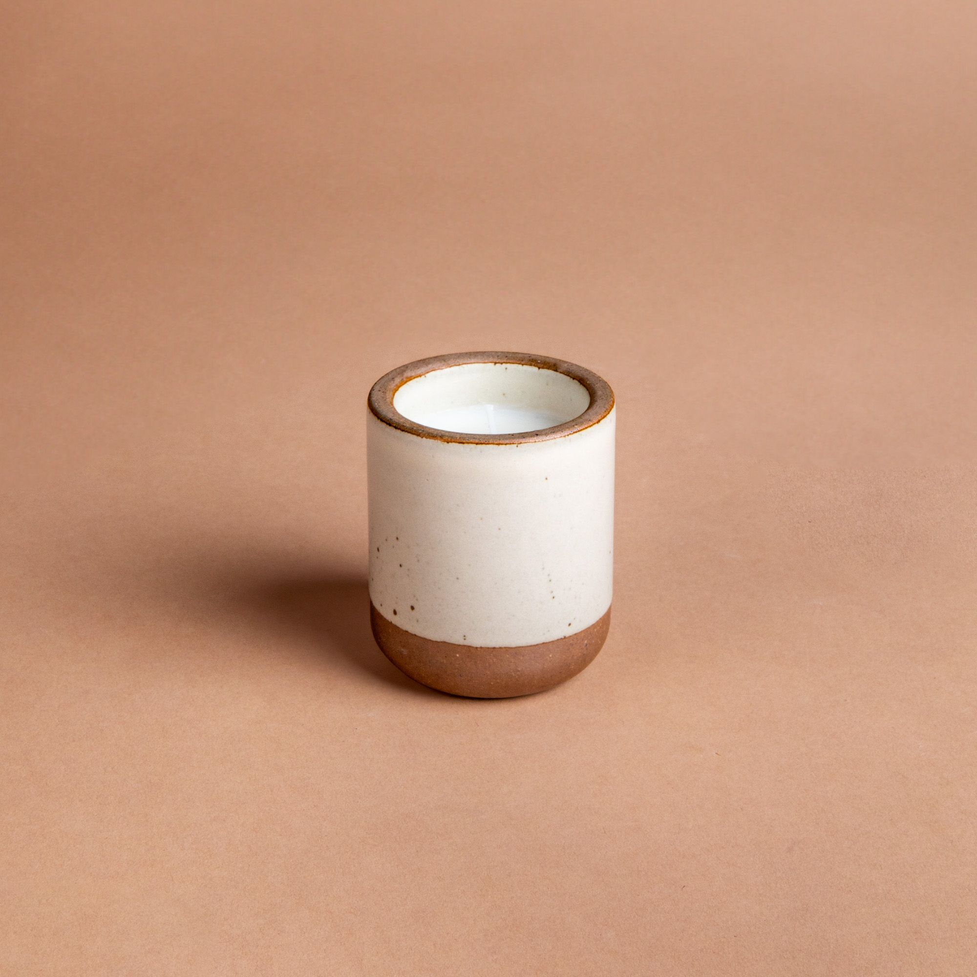 Small ceramic vessel in a warm off-white color with candle inside.