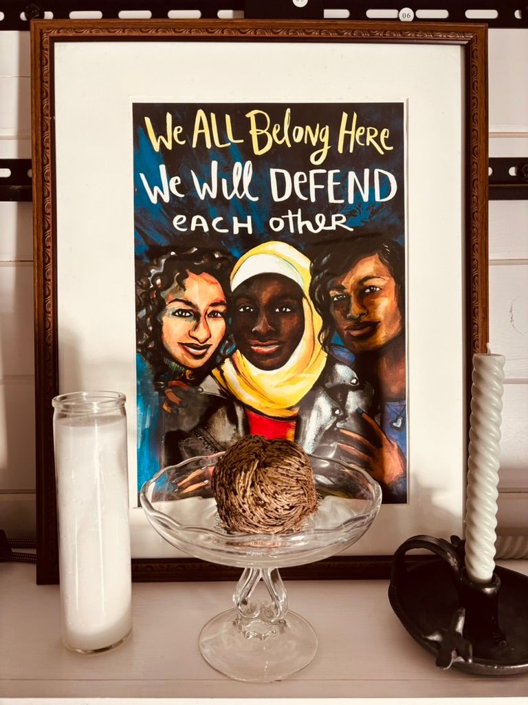 A framed photo reading 'We all belong here. We will defend each other.' sits on a white surface.