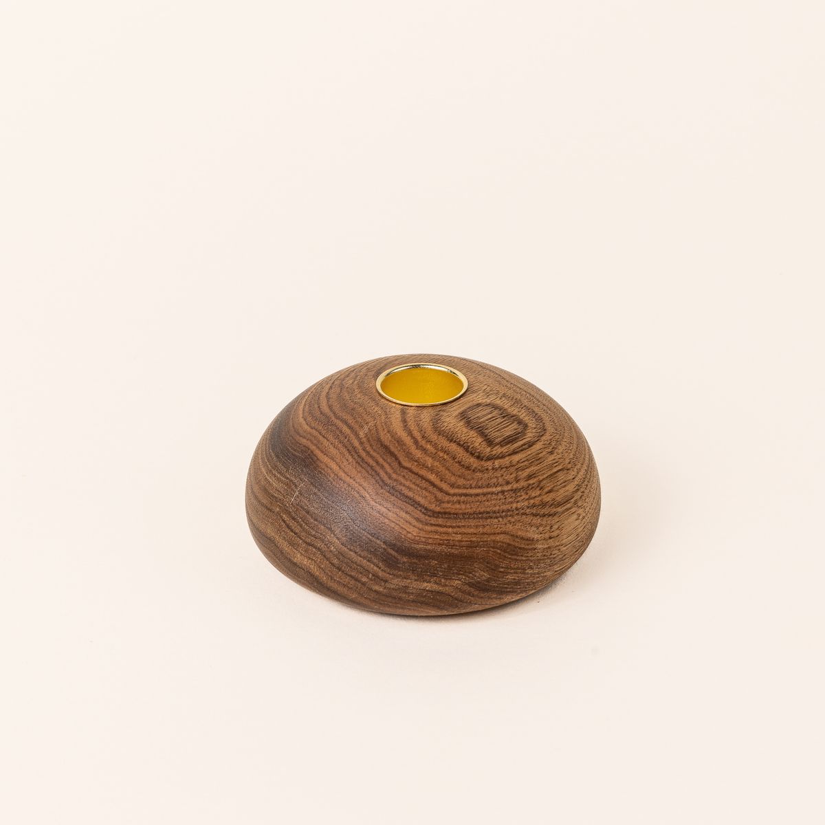 A butternut wood candle holder that is shaped like a small dome with a gold carved circle on top to hold the candle