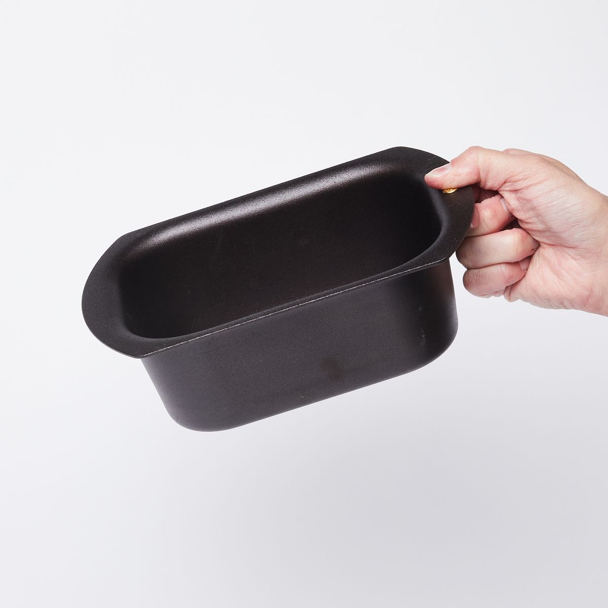 Hand holding a black metal loaf pan with rounded corners from the wide flat lip