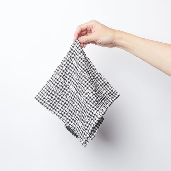 Hand holding a single black and white gingham cotton napkin from the corner