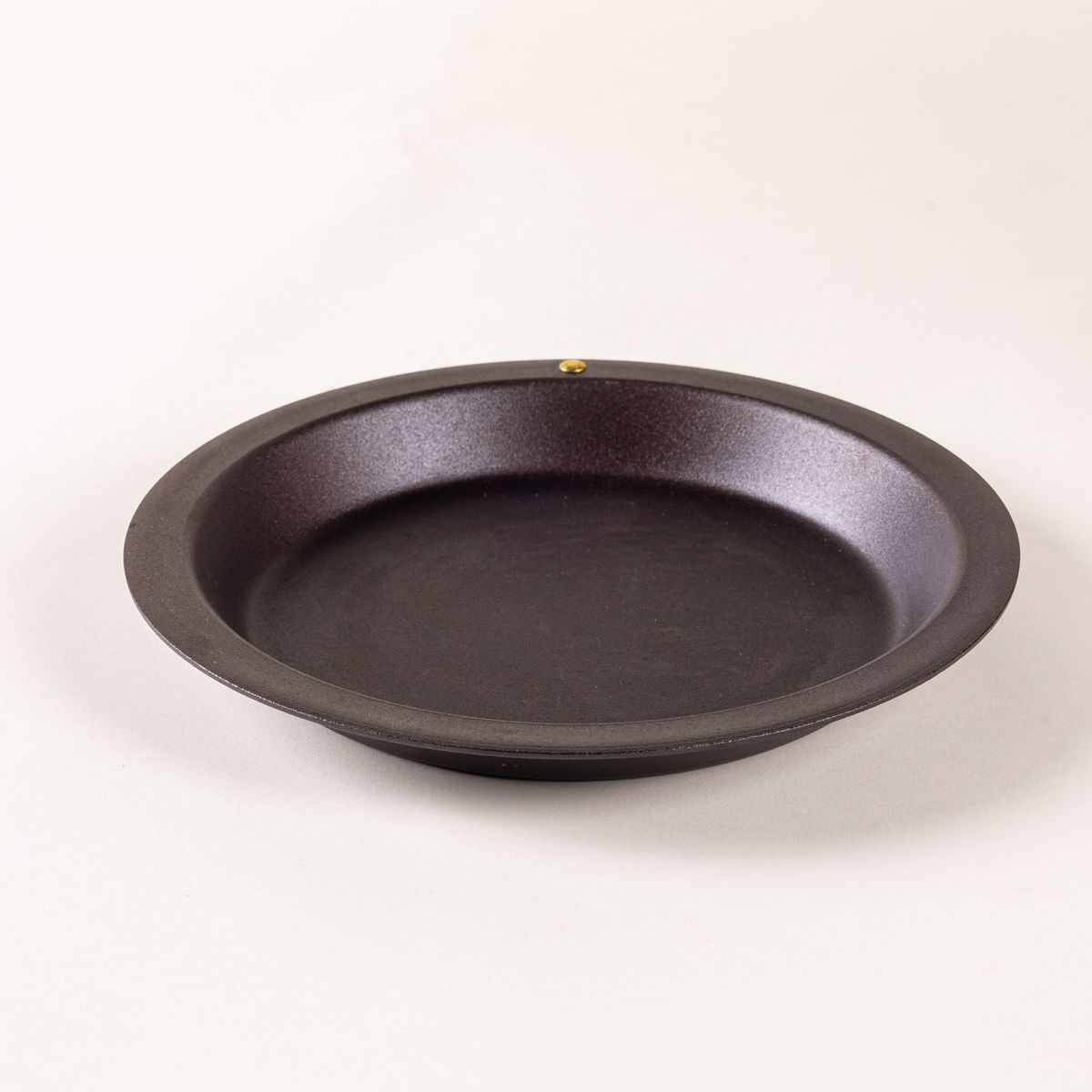 A simple iron pie dish with a wide rim and shallow body