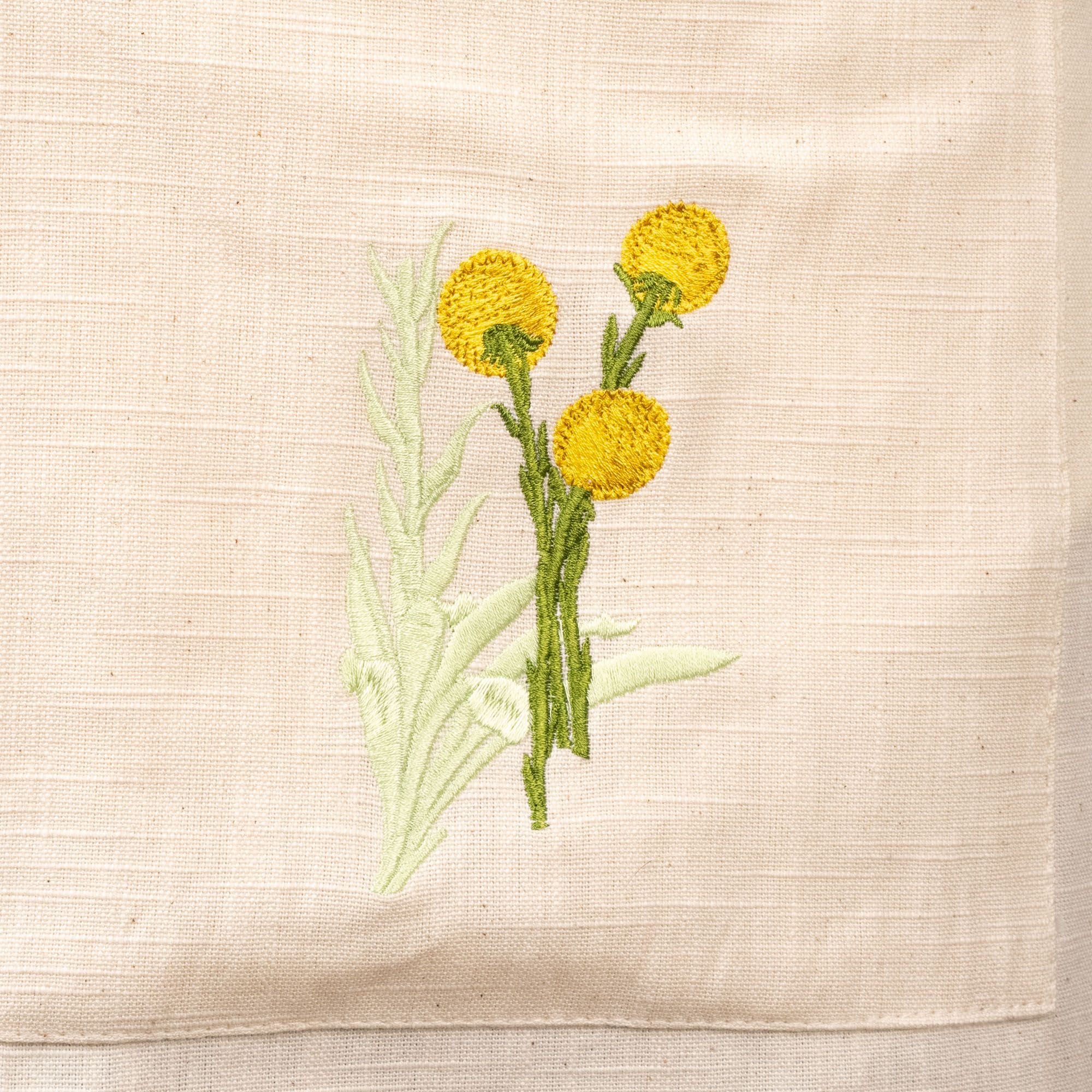 A close up of a green and yellow embroidered flower on a canvas apron.