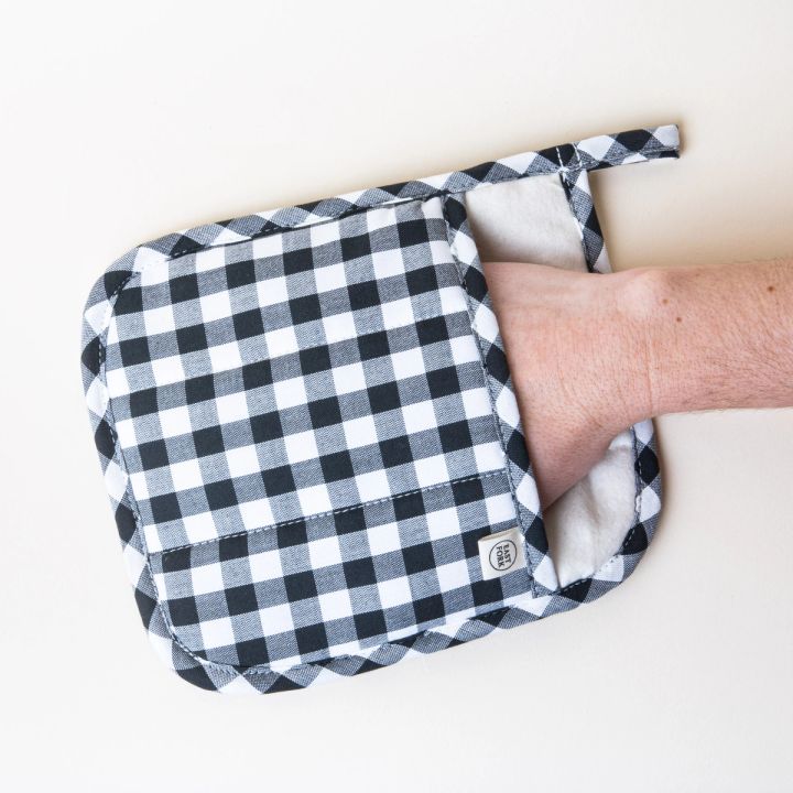 A hand inside a square pot holder made of black and white gingham fabric, with a little loop on the top left for hanging