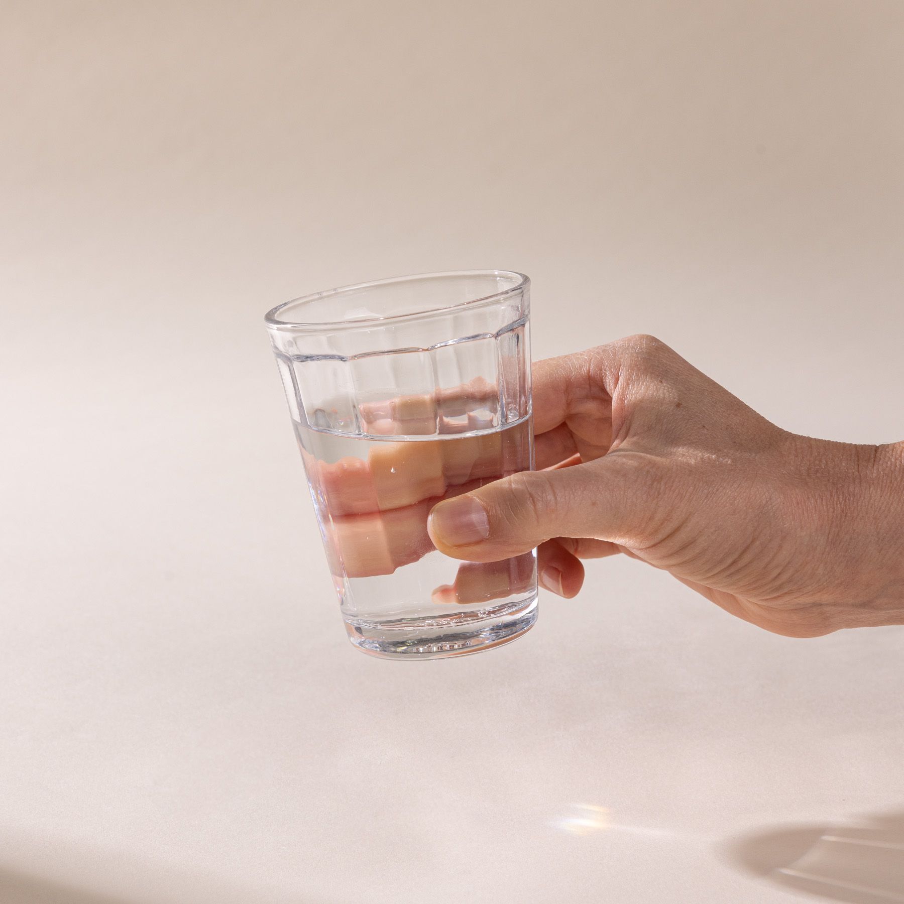 A hand holds a medium diner-style glass that tapers to be wider at the top, filled with water