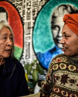 Two people are turned and looking at each other in the middle of a discussion in front of a vibrant mural