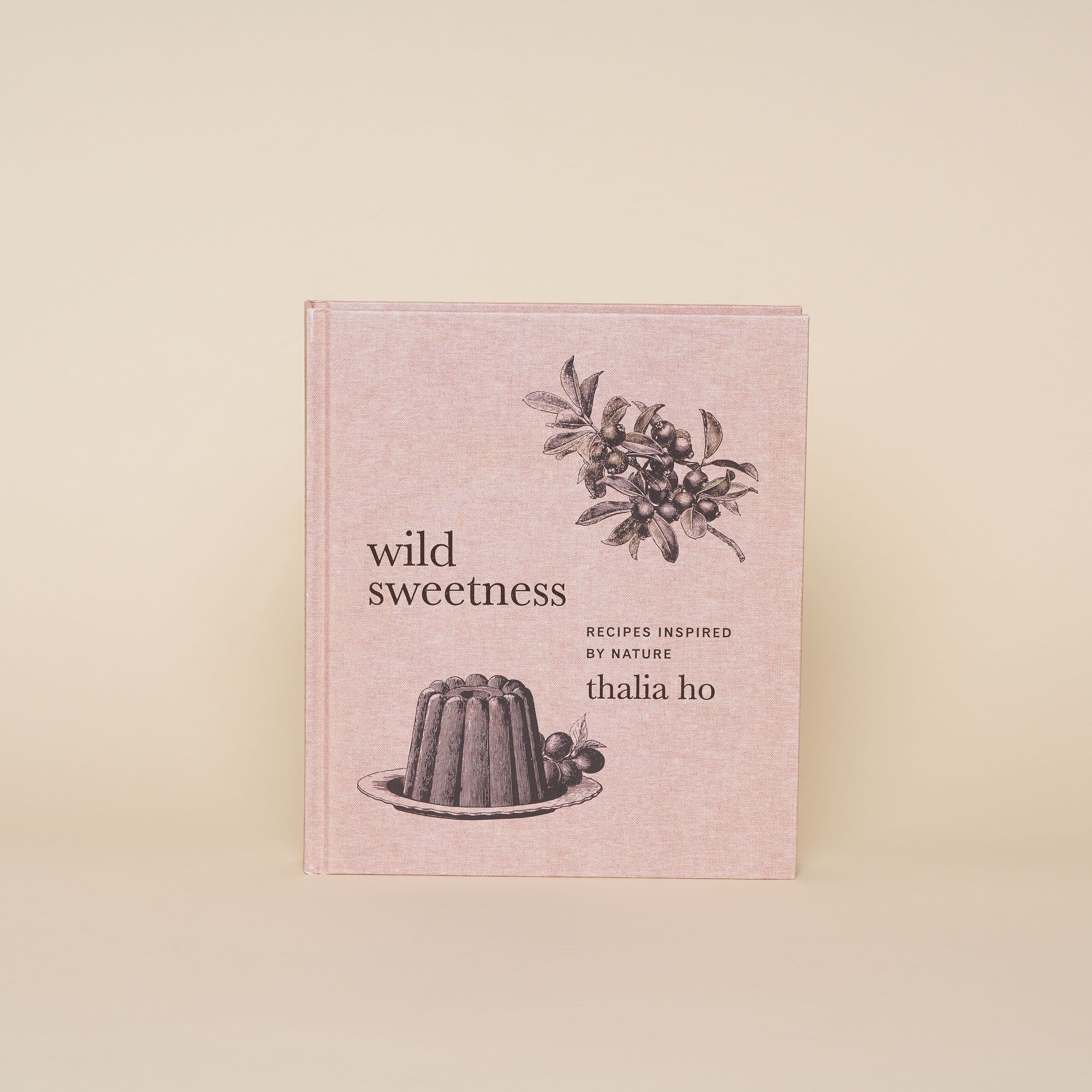 A hardcover cookbook with a pastel pink cover with an illustration of a bunt cake with other floral elements