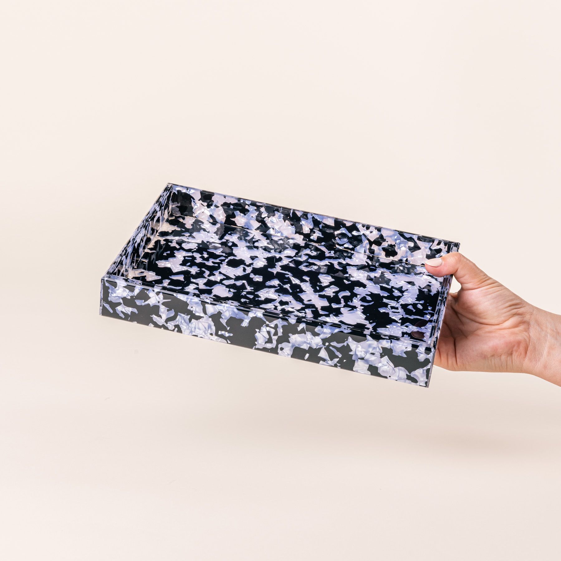 A hand holds a rectangular acrylic tray with a black and light blue granite-like design