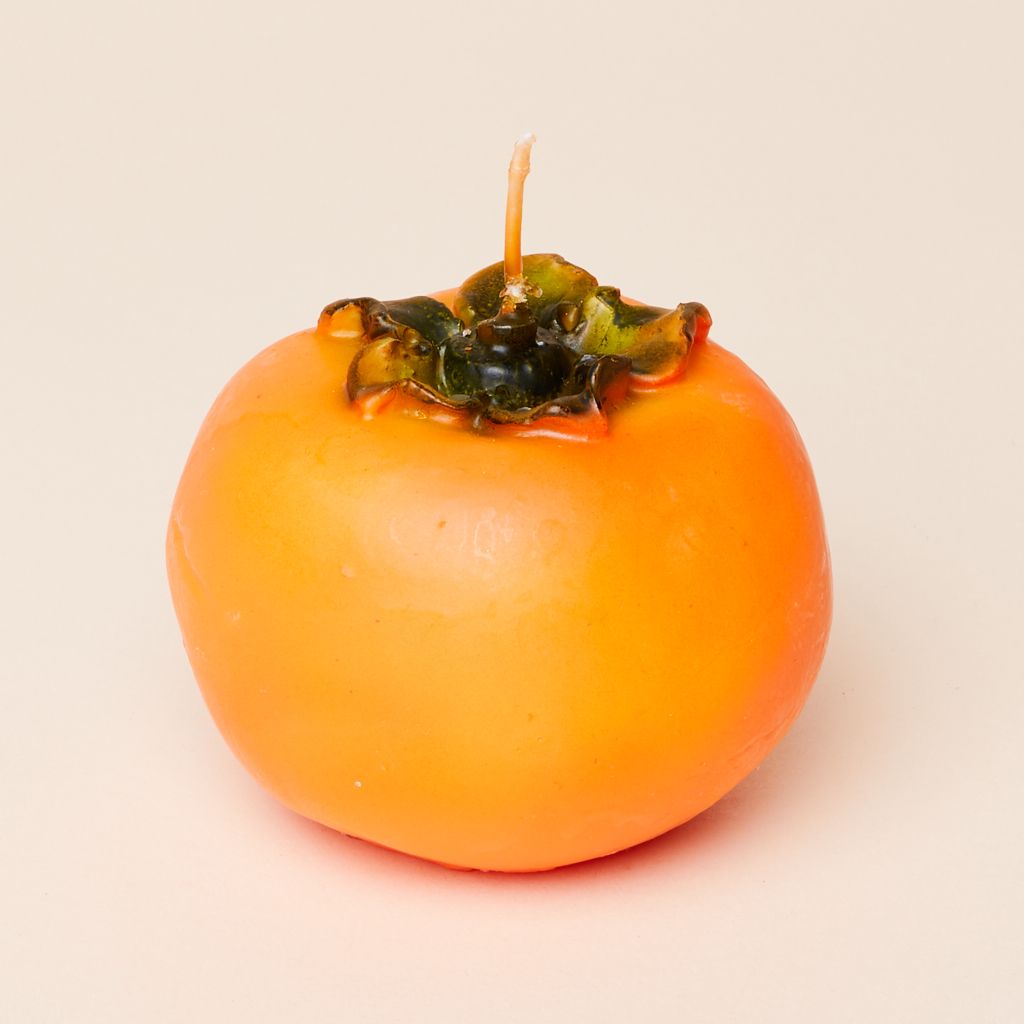 A round orange candle with green texture at the top, to suggest a whole persimmon