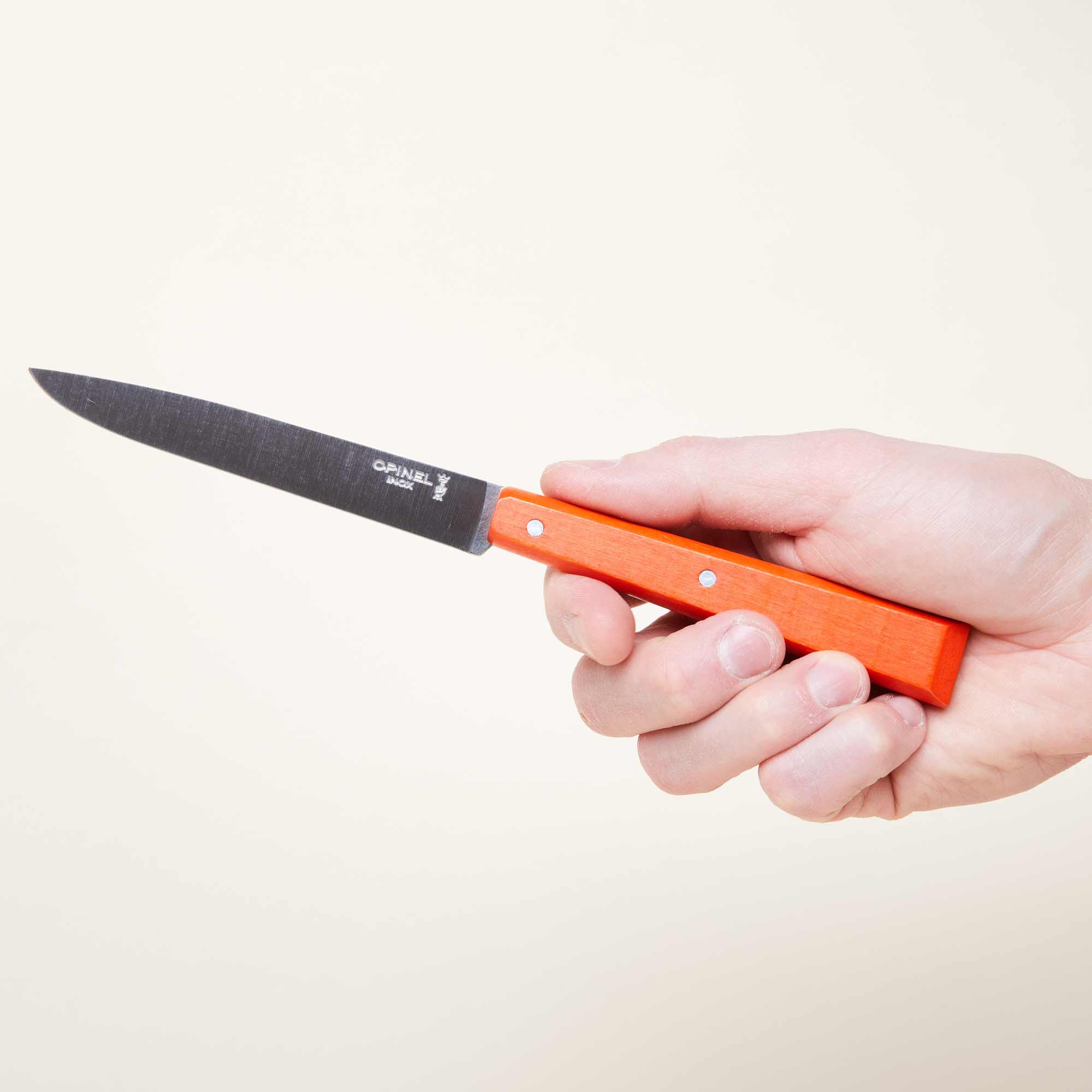 A hand holds a steak knife with a bold orange handle