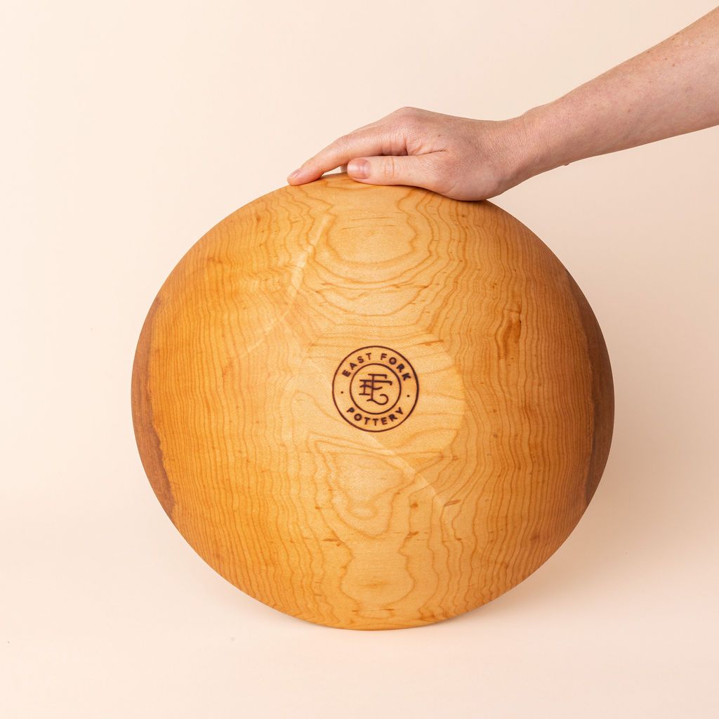 A hand showing off the bottom of a handcrafted wooden maplewood bowl that has an engraved stamp on the bottom that reads, "East Fork Pottery".