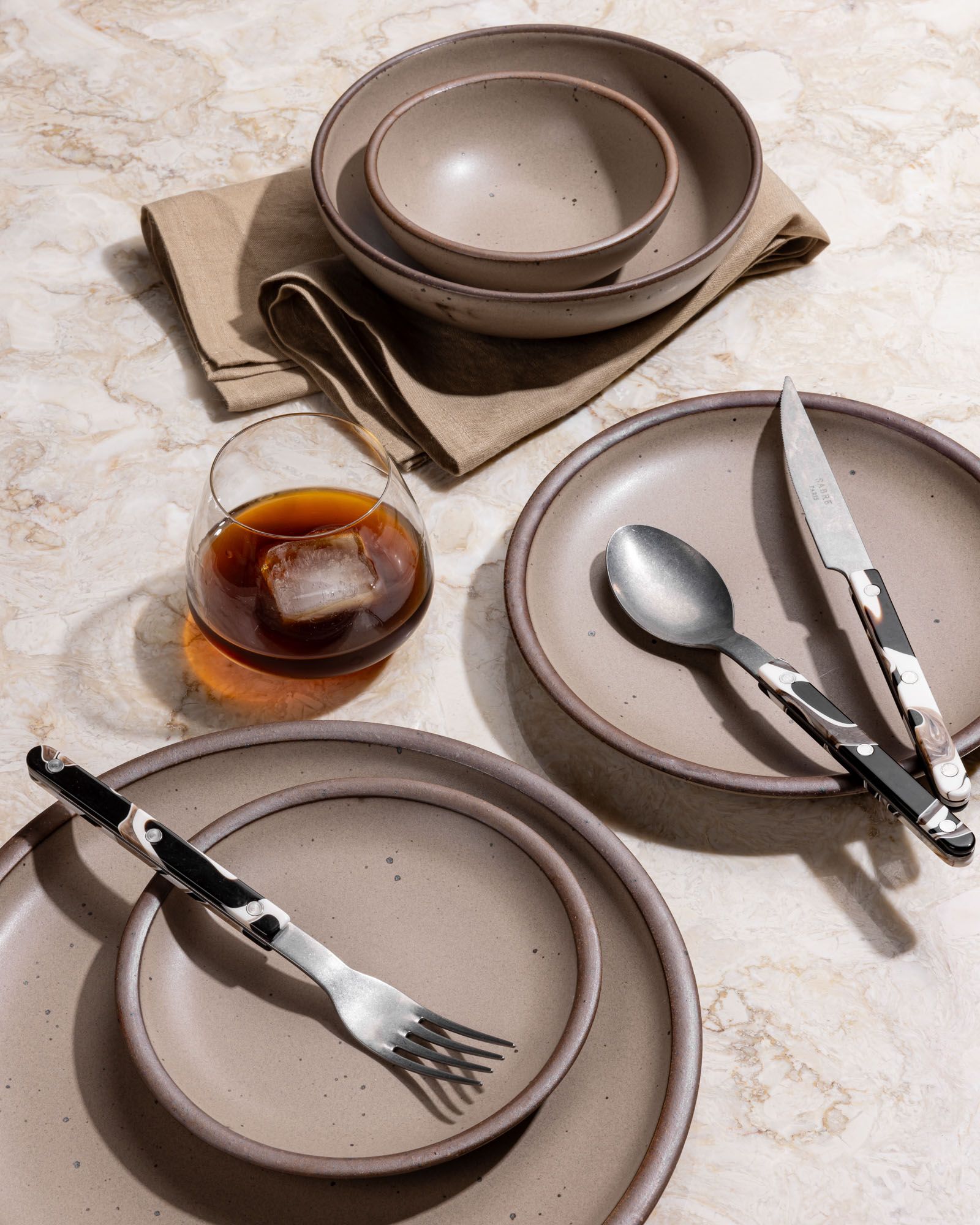 Various ceramic plates and bowls in various sizes in a warm tan-toned brown color, with marbled flatware