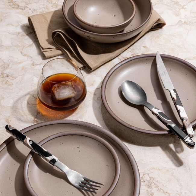 Various ceramic plates and bowls in various sizes in a warm tan-toned brown color, with marbled flatware