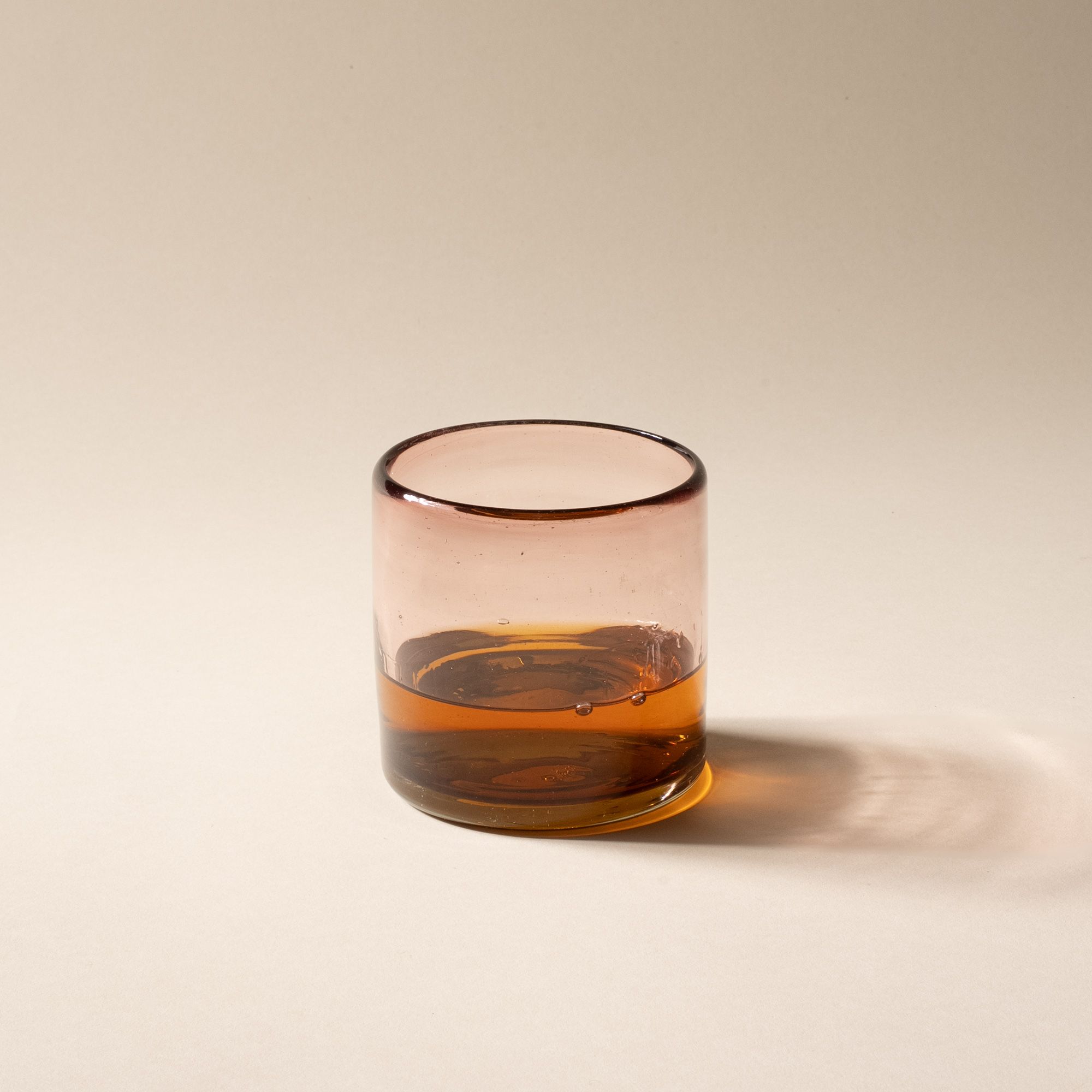 A light plum short transparent drinking glass with whiskey inside