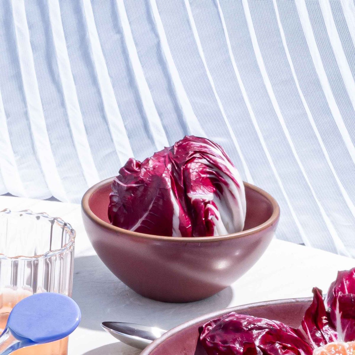 A small dessert sized rounded ceramic bowl in a plum color with red lettuce leaves inside