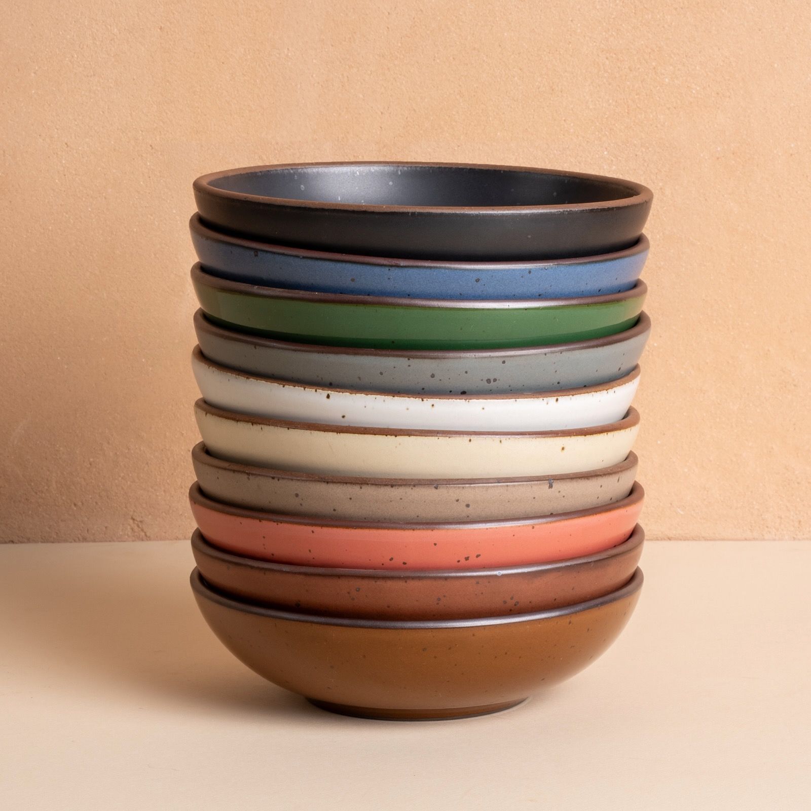 A stacked set of ceramic bowls in assorted colors—black, blue, green, gray, white, cream, brown, coral, and rust—forming a rainbow-like gradient.