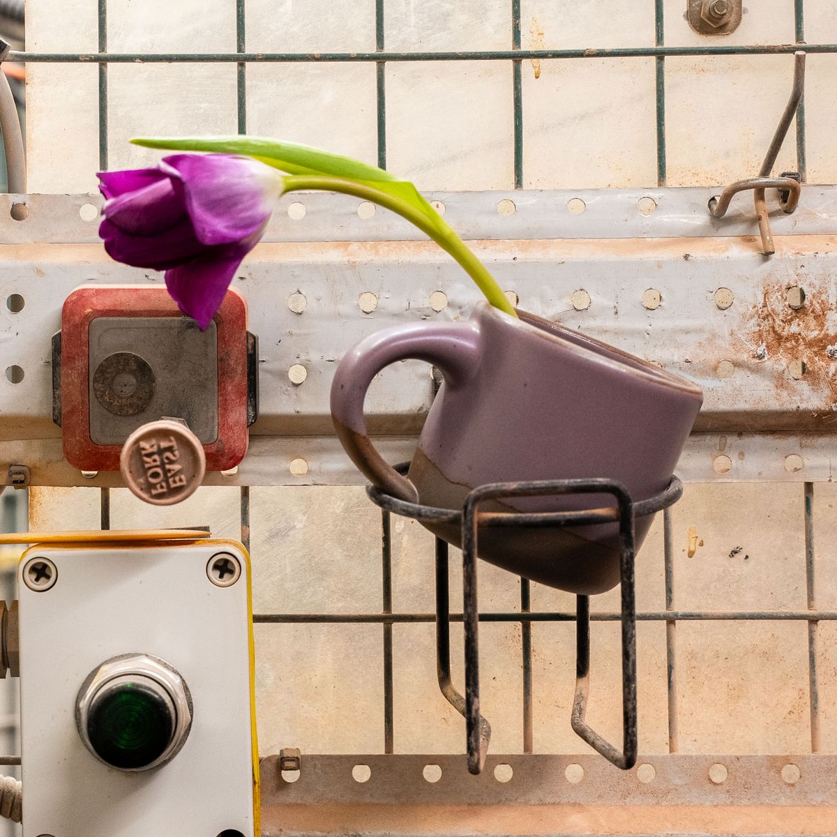 The Small Mug in a soft mauve purple color, sitting in a ceramic factory with a bright purple flower coming out.