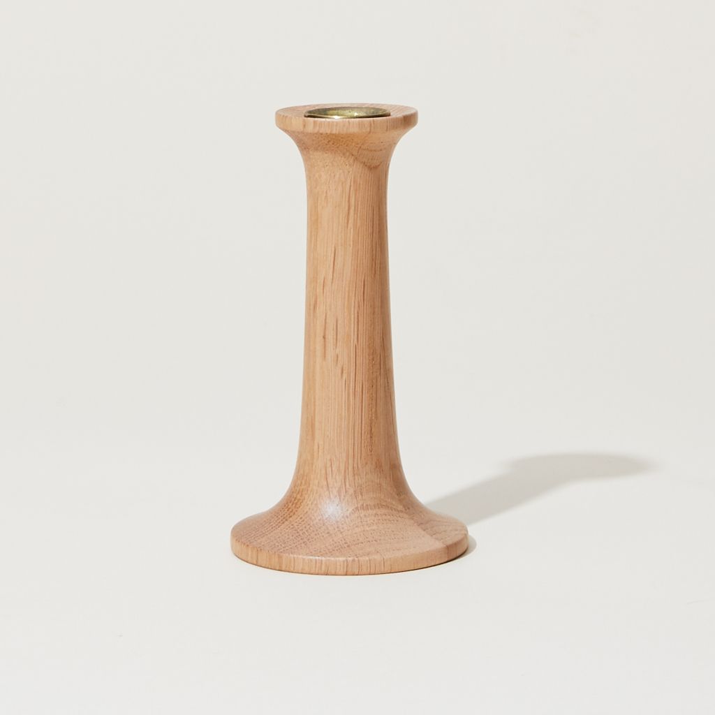 Thin light wood cylinder with a slightly wide base with a yellow taper candle sitting on top