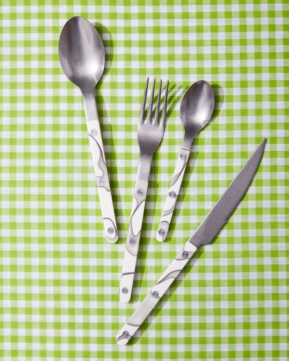 A soup spoon, dinner fork, teaspoon, and knife with white marbled handles sit against a lime gingham backdrop.