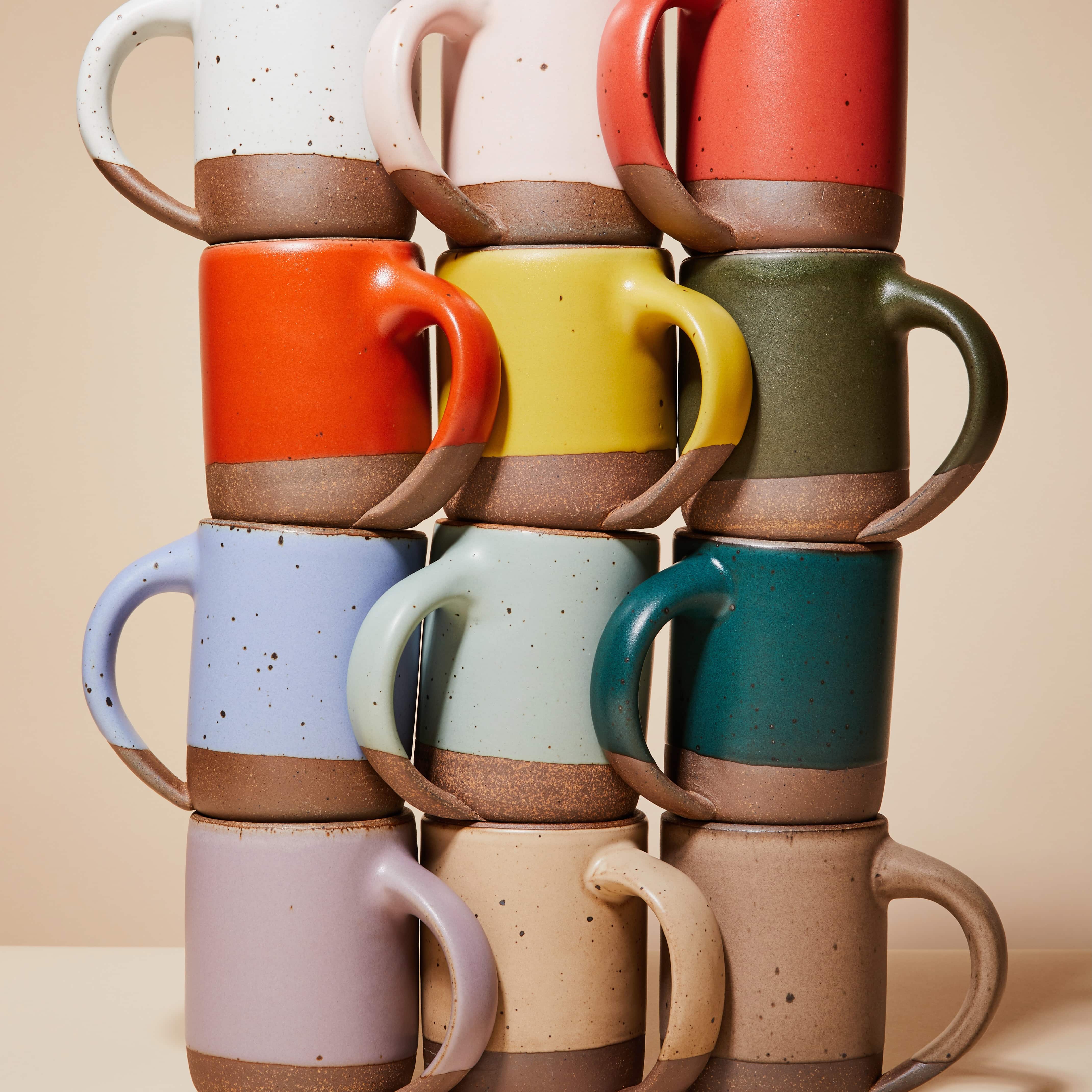 A stack of mugs - in rows of 3 in 4 columns - each mug has a different color resulting in a rainbow.