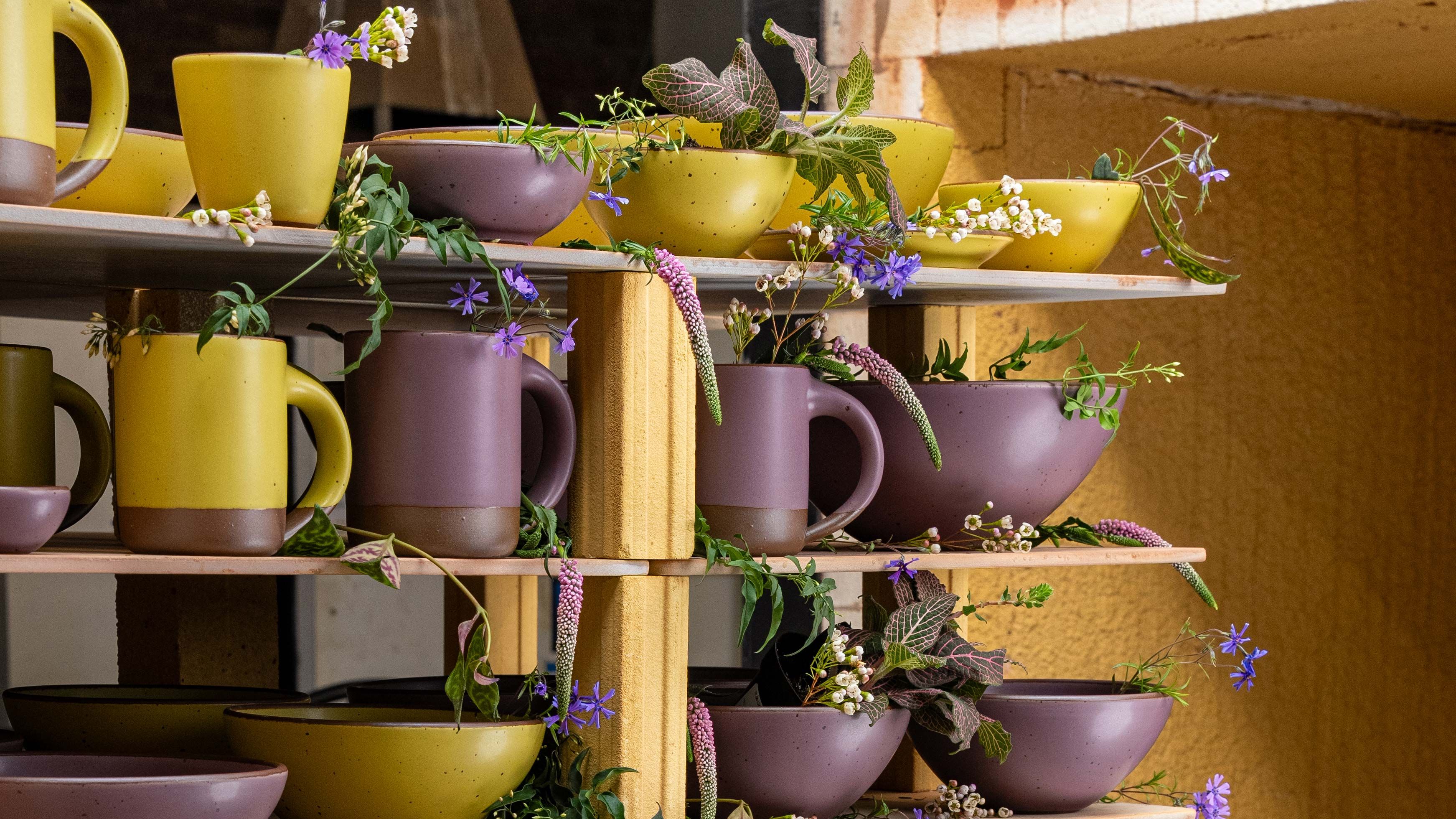 A table filled with ceramic pottery in periwinkle and plum colors, a salad, and glasses filled with orange liquid