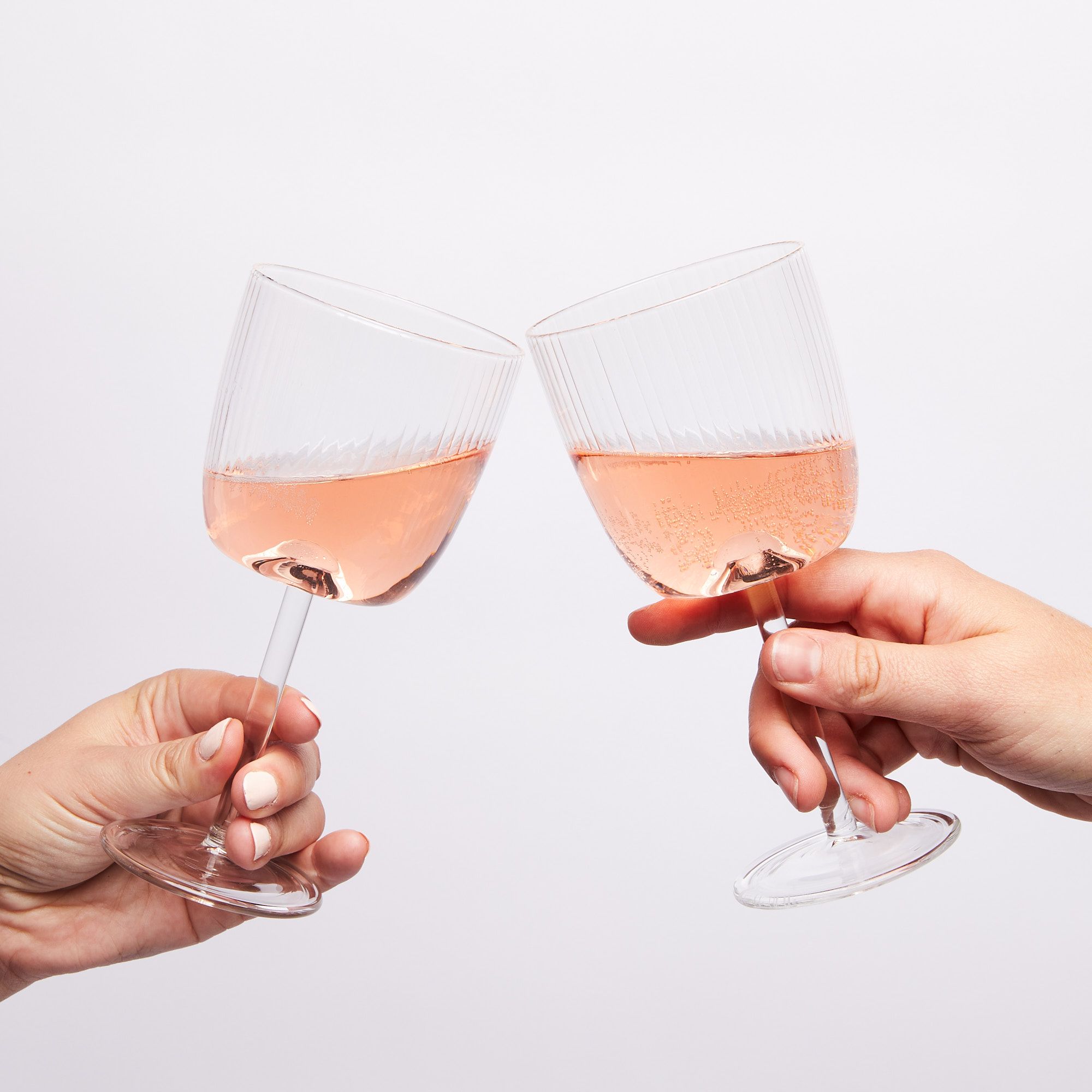 Hands holding two wine glasses with pink wine half full cheersing
