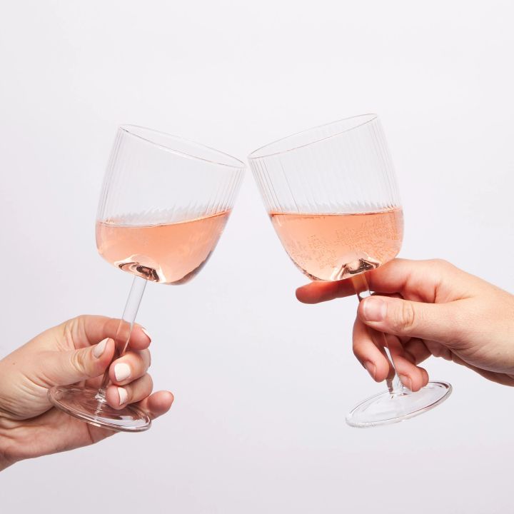two hands cheersing two wine glasses with pink wine