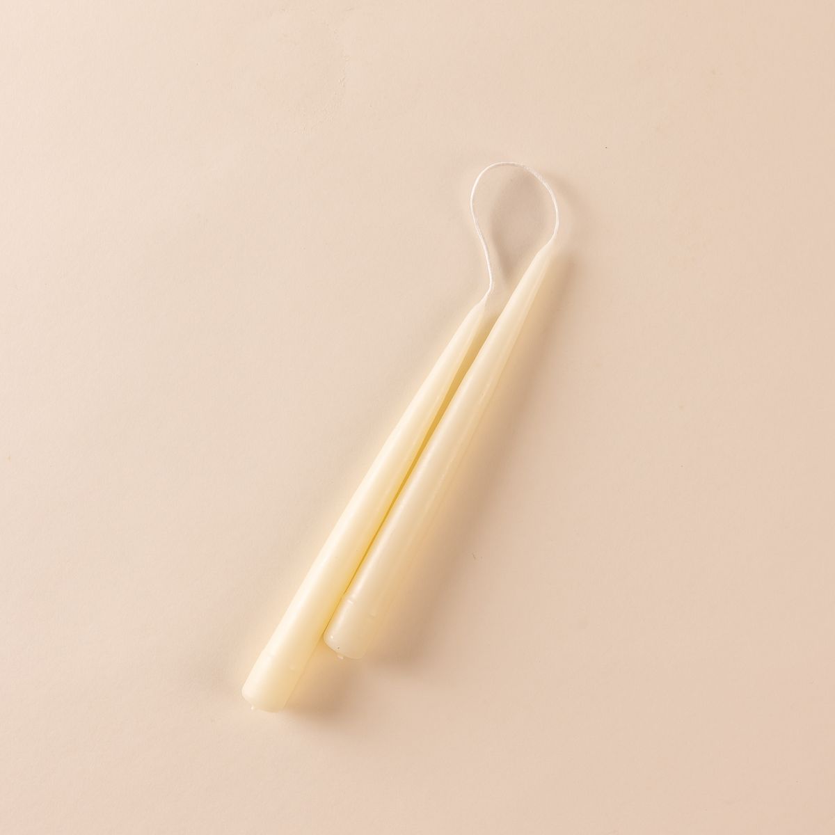 A pairs of cream taper candles with the wick connected at the top.