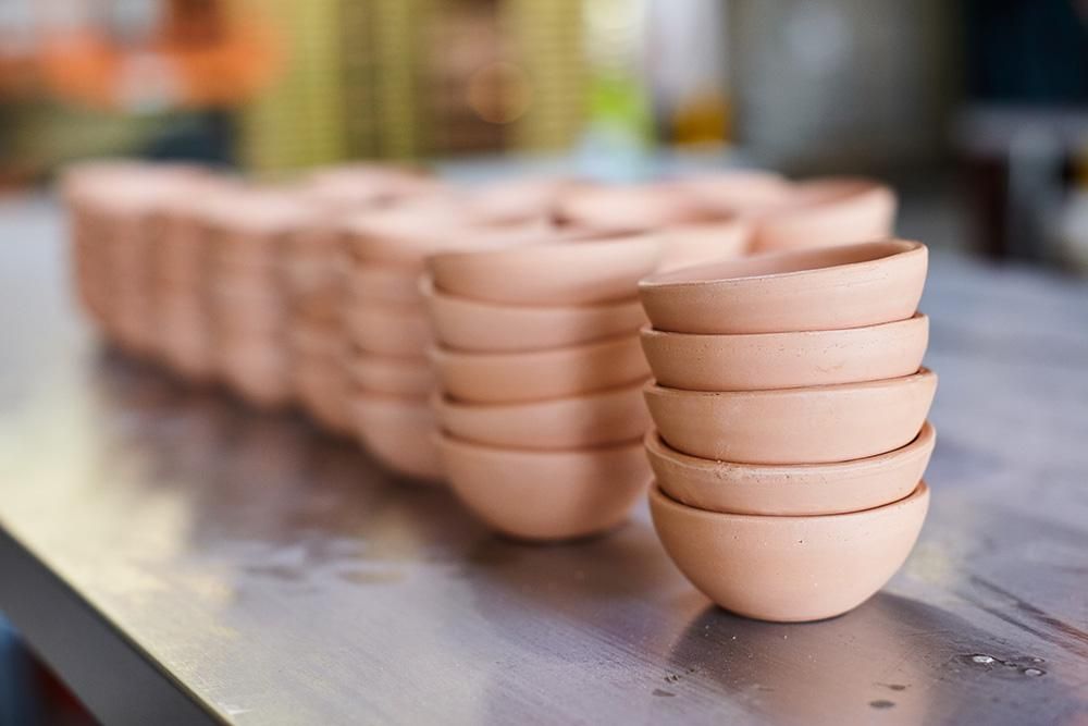 Rows of unglazed stacks of bitty bowls are sitting on a metal table.
