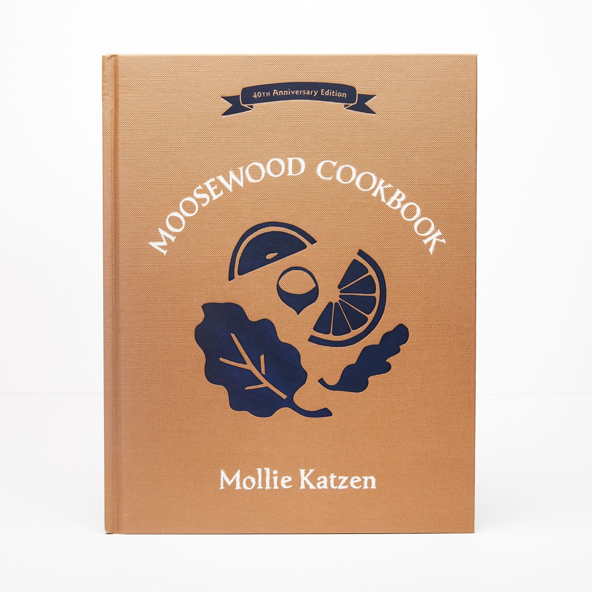 A book with a kraft brown color and silhouette illustrations of leaves and fruit slices with a title that reads "Moosewood Cookbook"