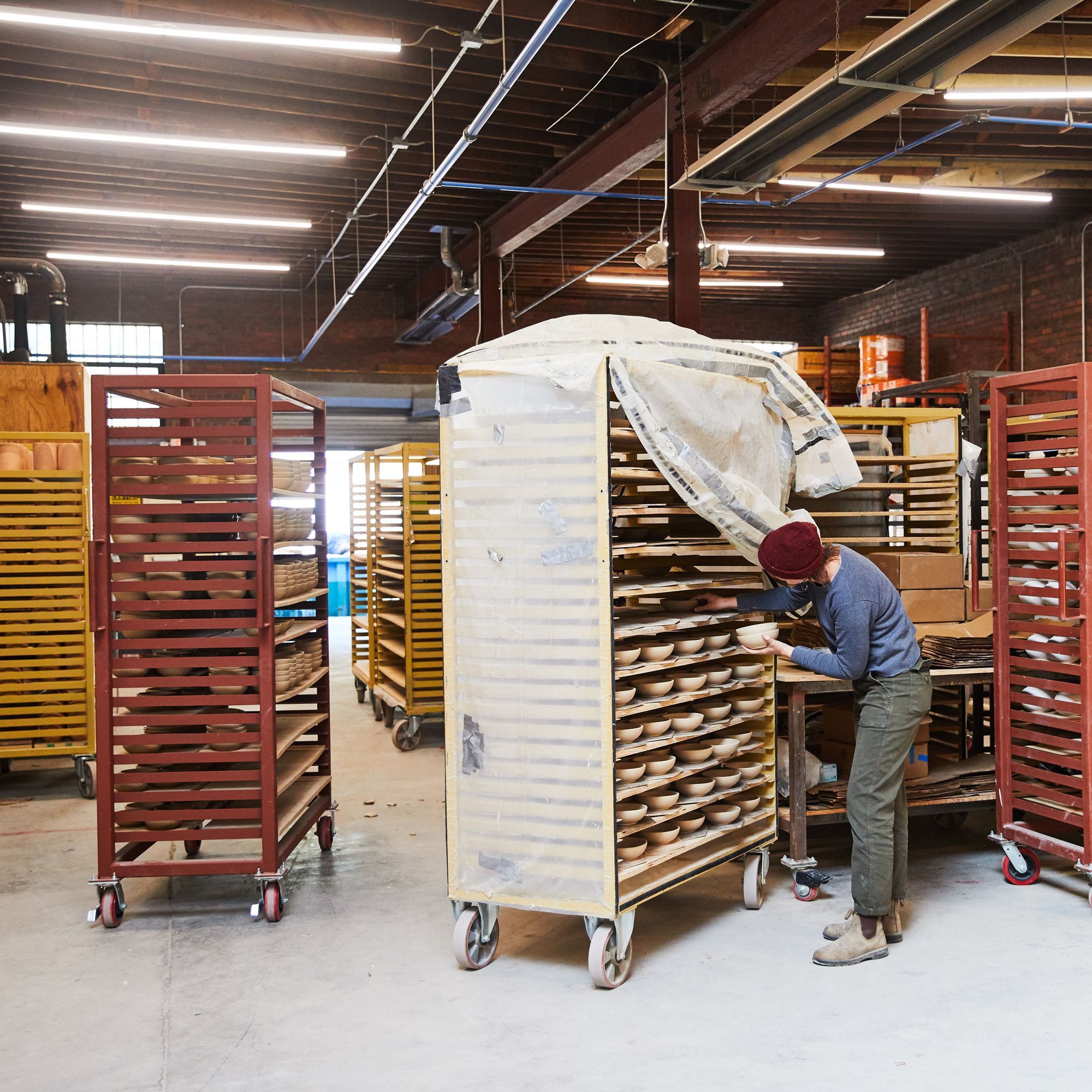 A person loading kiln carts with bisque pottery in a factory setting