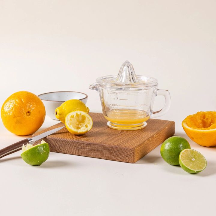 A traditional glass juicer with a handle and juice inside, surrounded by slices of limes, lemons, and oranges.