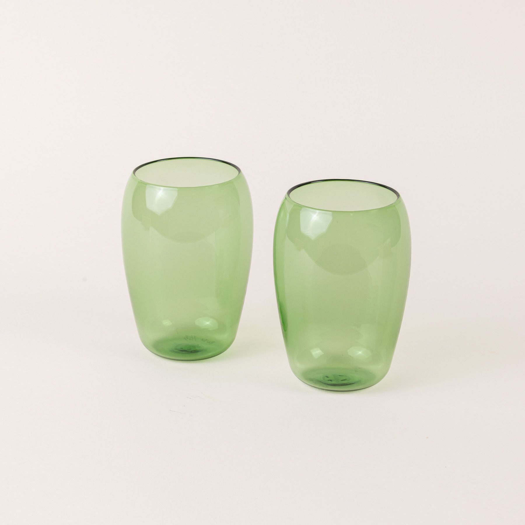 Two tall light green glass tumblers with a slight curve inward on the top.