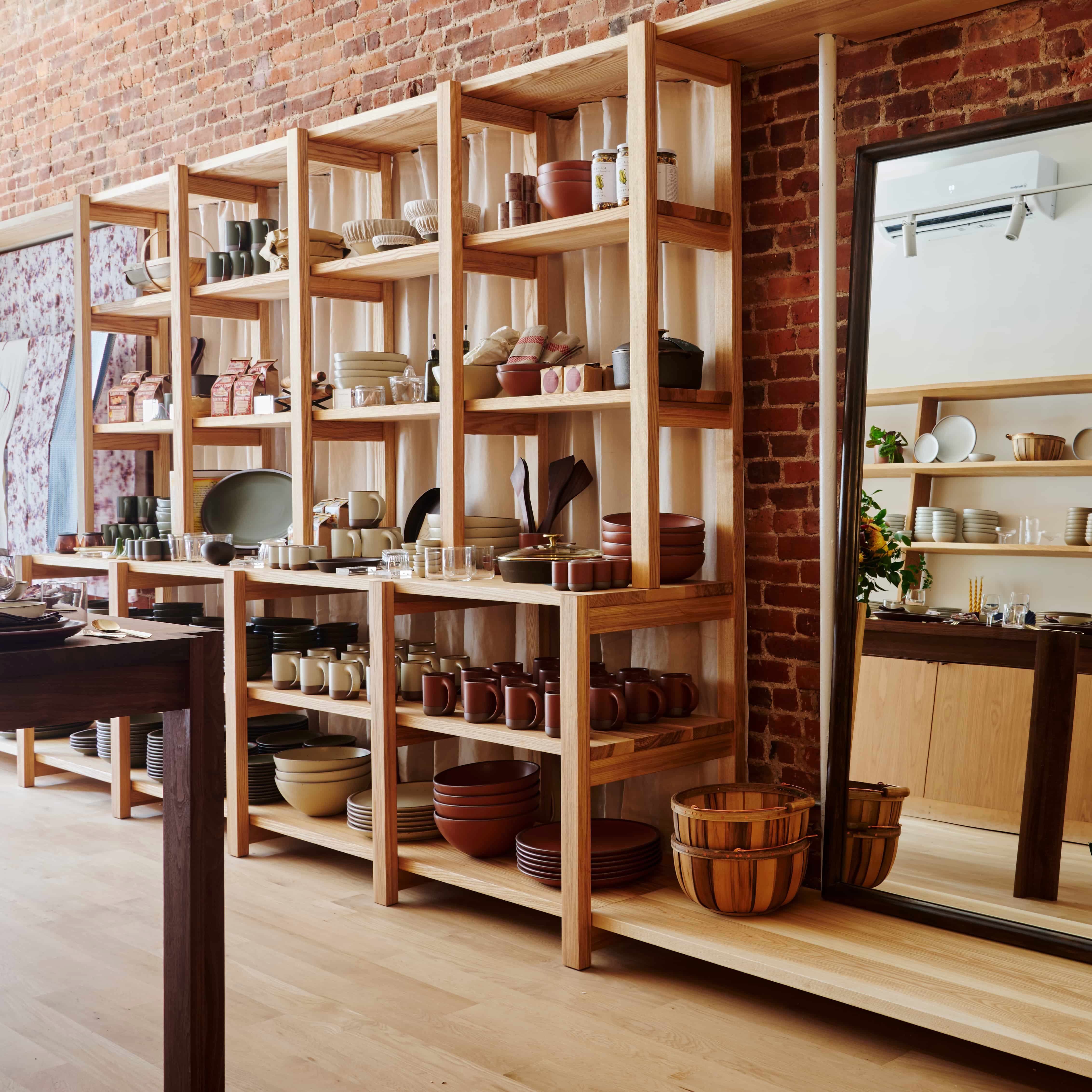 A long built in shelf against a brick wall with a mirror and ceramic bowls and plates fill the shelves