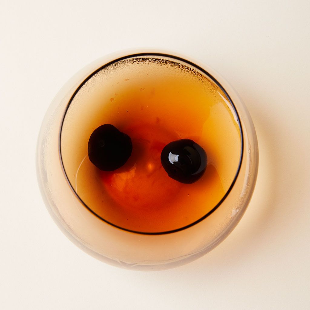 Overhead view of a glass that contains two darkest red cherries in an amber liquid