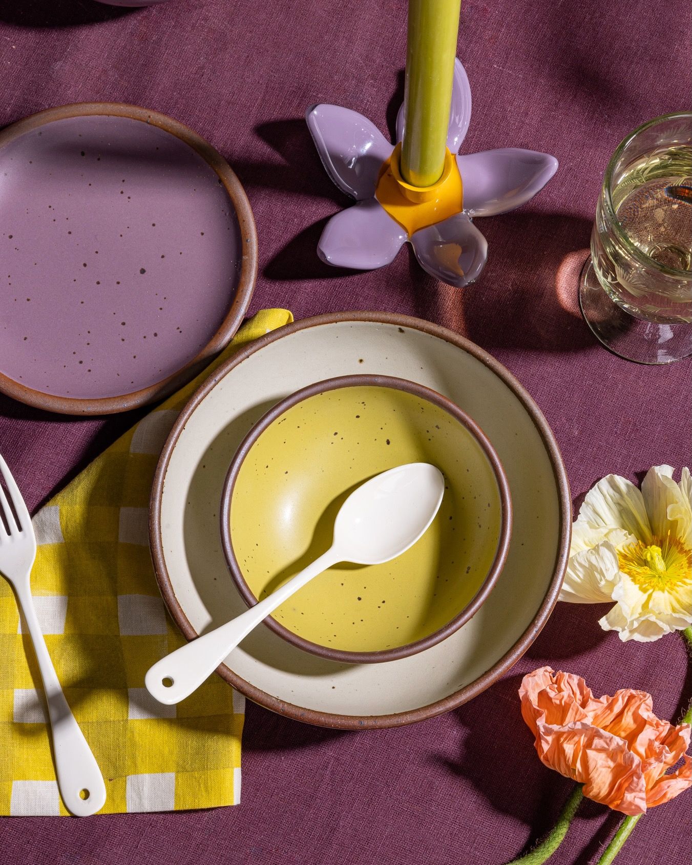 A small dessert sized rounded ceramic bowl in a zesty yellow color nestled in a larger cream ceramic bowl with an enamel spoon, and yellow and purple table linens.