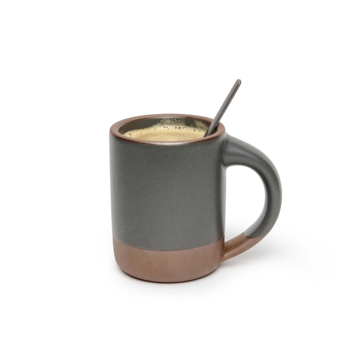 A medium sized ceramic mug with handle in a cool, medium grey color featuring iron speckles and unglazed rim and bottom base, filled with coffee and a spoon