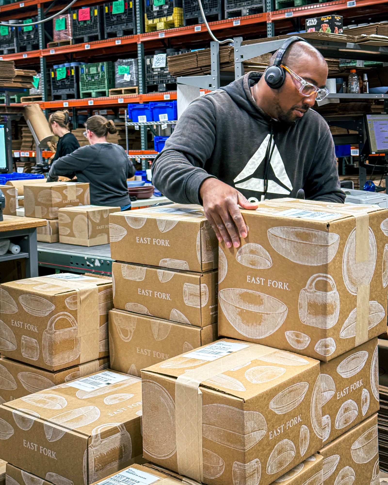 In a factory setting, employees are packing East Fork boxes and stacking them for shipment.