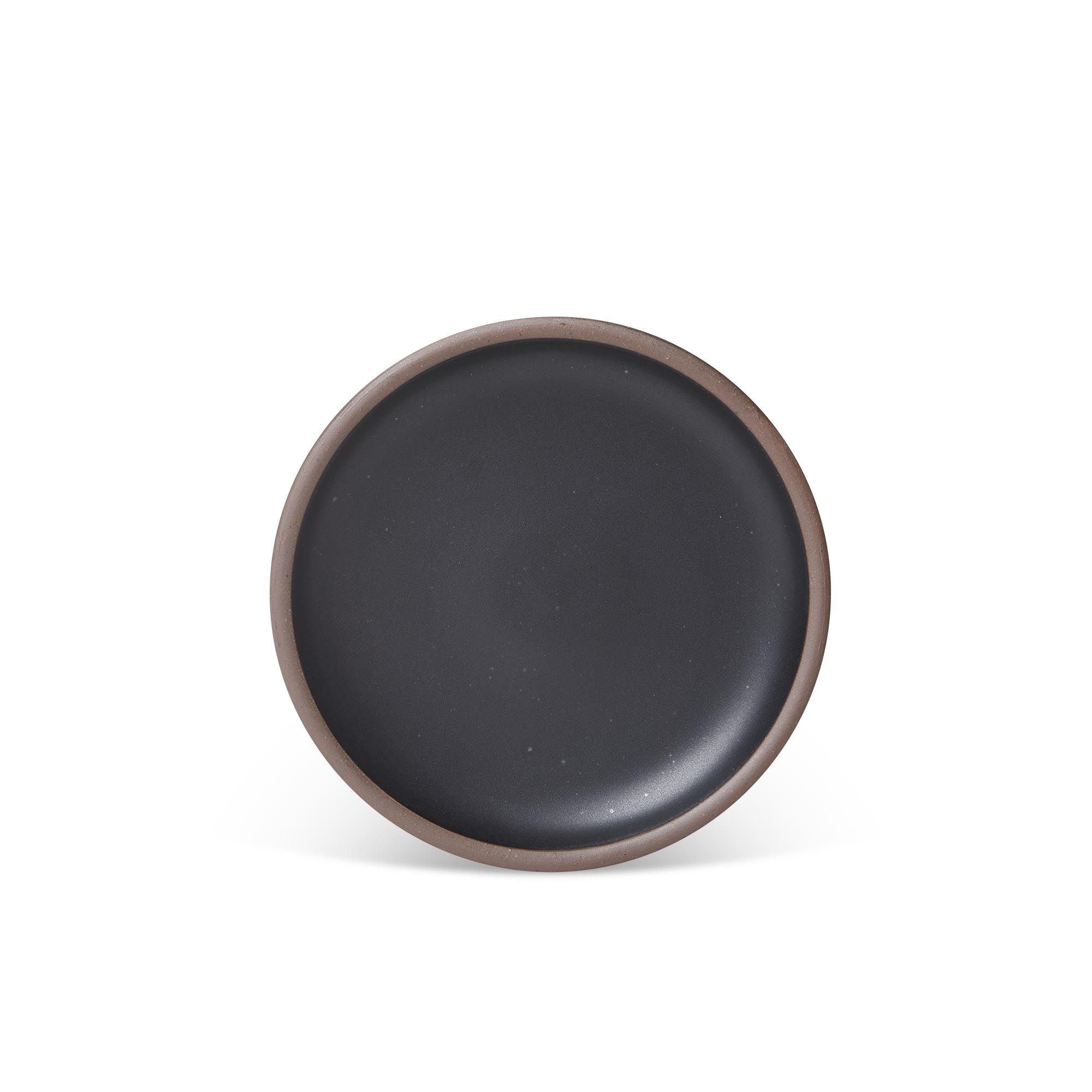 A medium sized ceramic plate in a graphite black color featuring iron speckles and an unglazed rim.