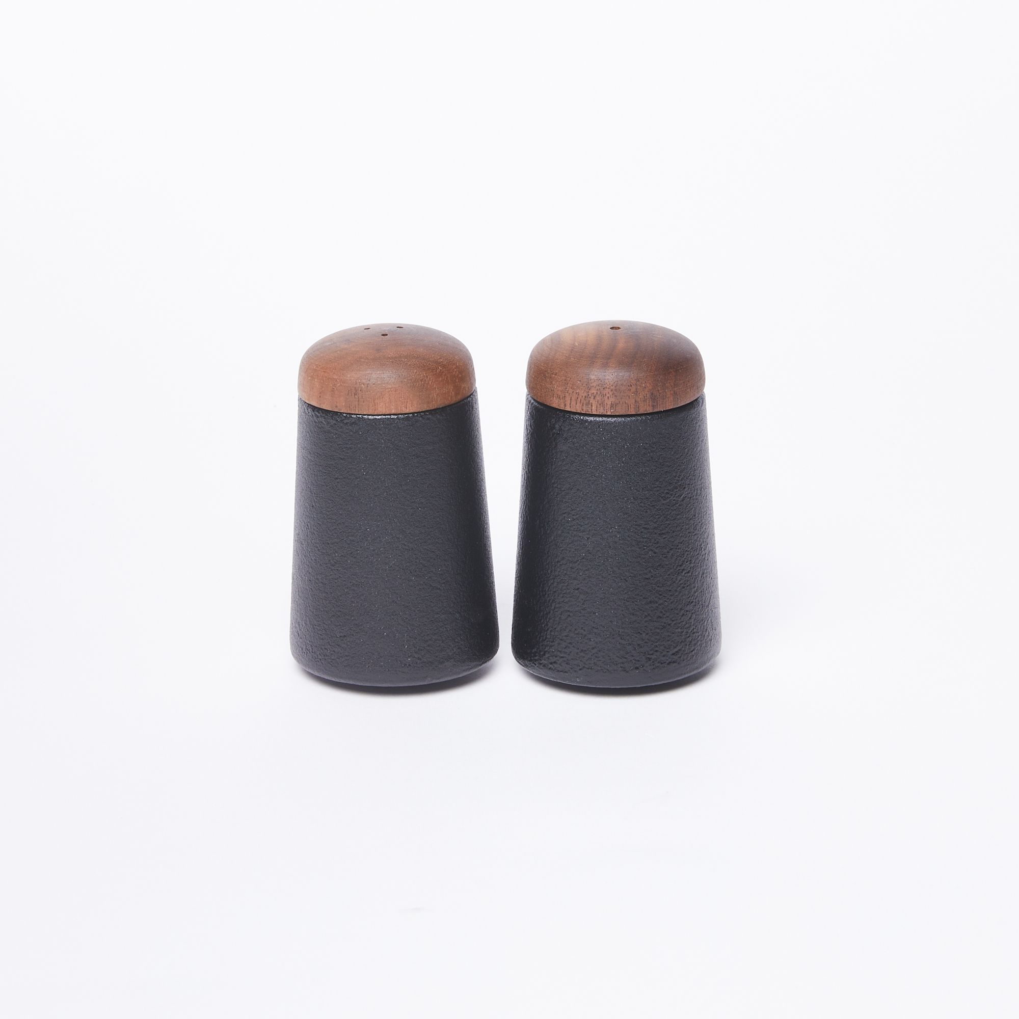 A set of salt and pepper shakers with a black cast iron base with a rounded walnut wood top on a white background