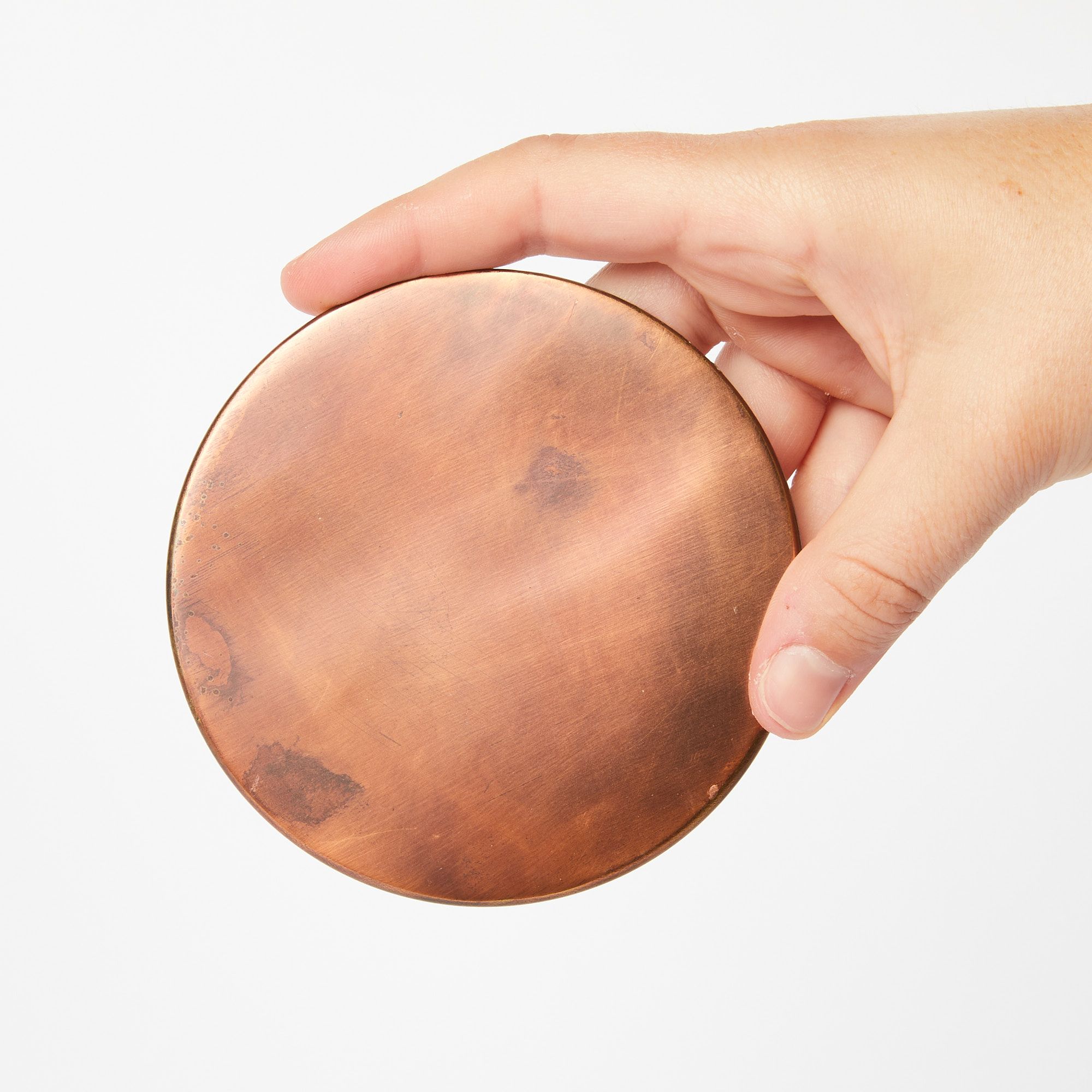 A hand holding a round copper coaster